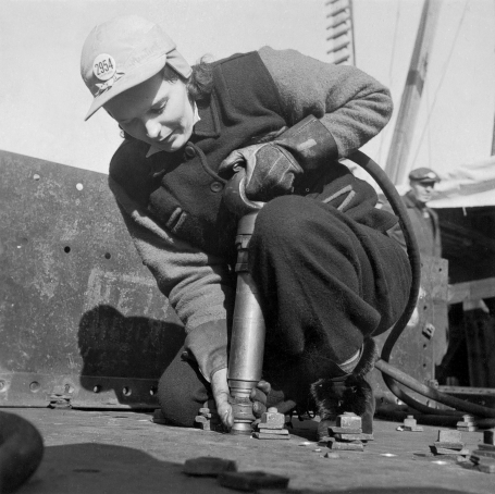 Photo of worker Mrs. A. Mackay kneeling to use a riveting gun at Pictou Shipyards Ltd, Nova Scotia, January 1943.