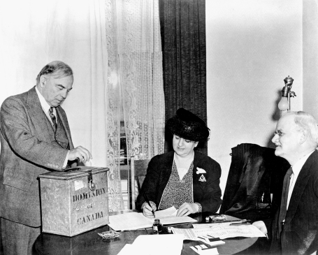 Photographed at the national plebiscite on April 27, 1942, Prime Minister W.L. Mackenzie King deposits his ballot in the box under the eyes of two supervisors in Ottawa, Ontario.
