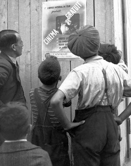 This photo shows a group of five citizens in front of a French poster announcing the free screening of NFB films in Lanoraie, Quebec, circa 1942.