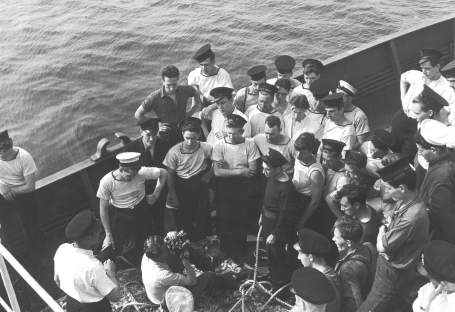 A film still from Corvette Port Arthur, showing a cameraman filming a group of sailors on the deck of the corvette.
