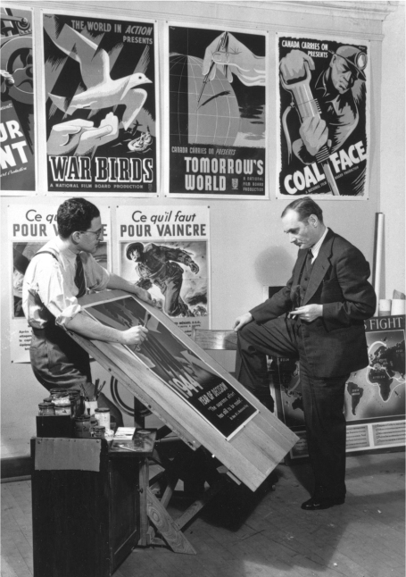 This photo shows John Grierson and Harry Mayerovitch standing in front of a wall covered in film and propaganda posters, discussing the design of a new poster lying on a drafting table.