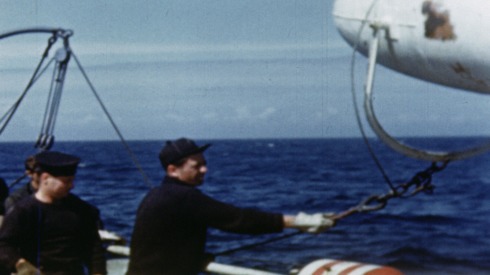 Colour footage : Signal flags being hoisted, buoys for minesweeper being laid, and being hauled onto deck by pulley (06/06/1944 or 07/06/1944).